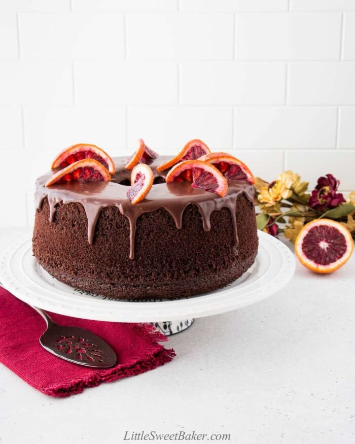 Chocolate chiffon cake topped with ganache and orange slices on a white cake plate.