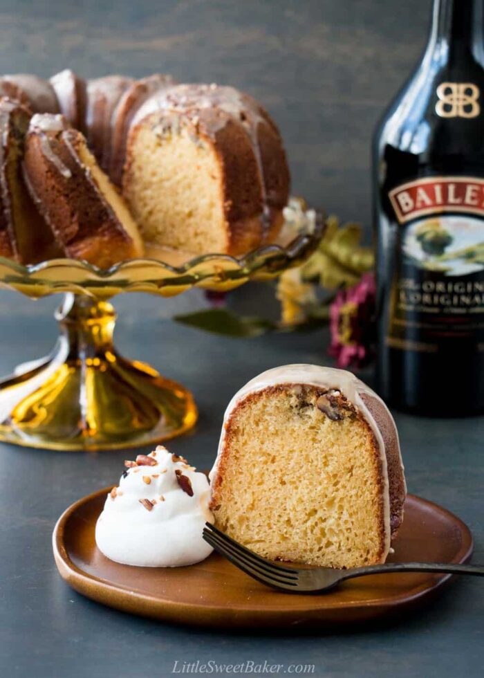 A slice of irish cream bundt cake on a wooden plate with a dollop of whipped cream.