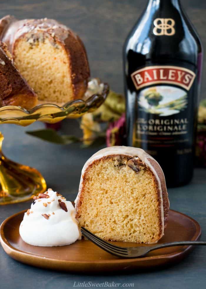 A slice of glazed Irish cream bundt cake on a wooden plate with whipped cream.