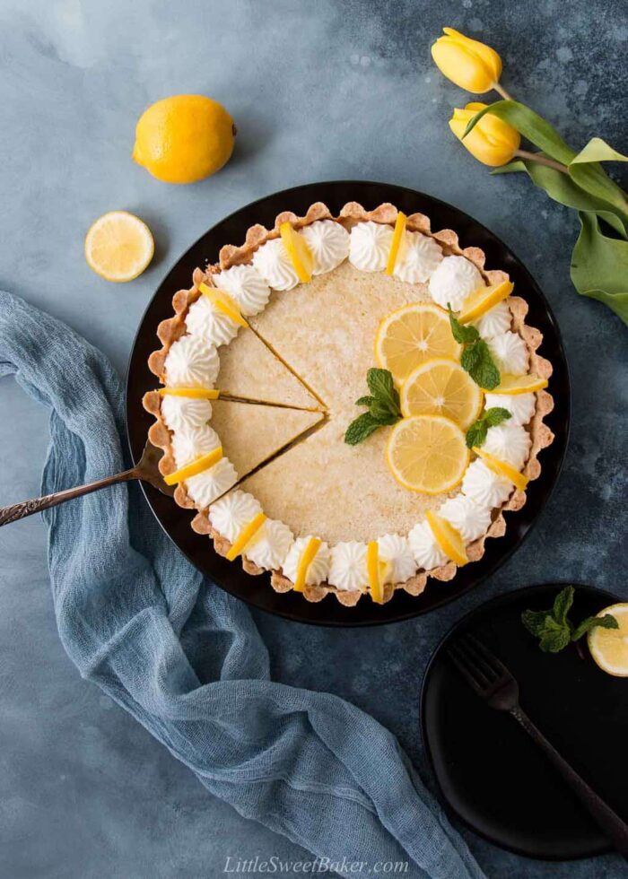 A lemon tart on a black plate with two slice cut.