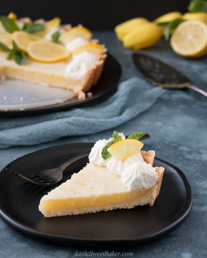 A slice of lemon tart on a black plate.