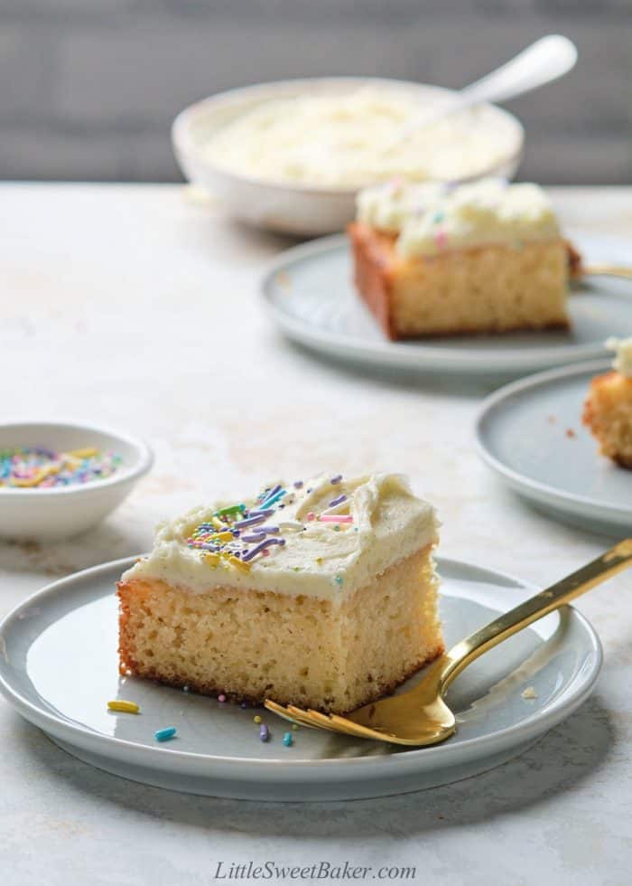 A slice of vanilla cake topped with vanilla buttercream and sprinkles on a light blue plate.