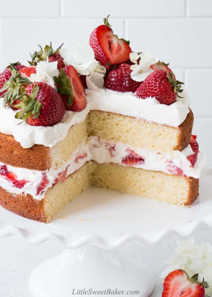 A strawberry shortcake layer cake with a quarter of the cake removed.