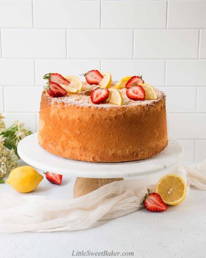 Lemon chiffon cake topped with strawberries and lemon slices on a white cake stand.