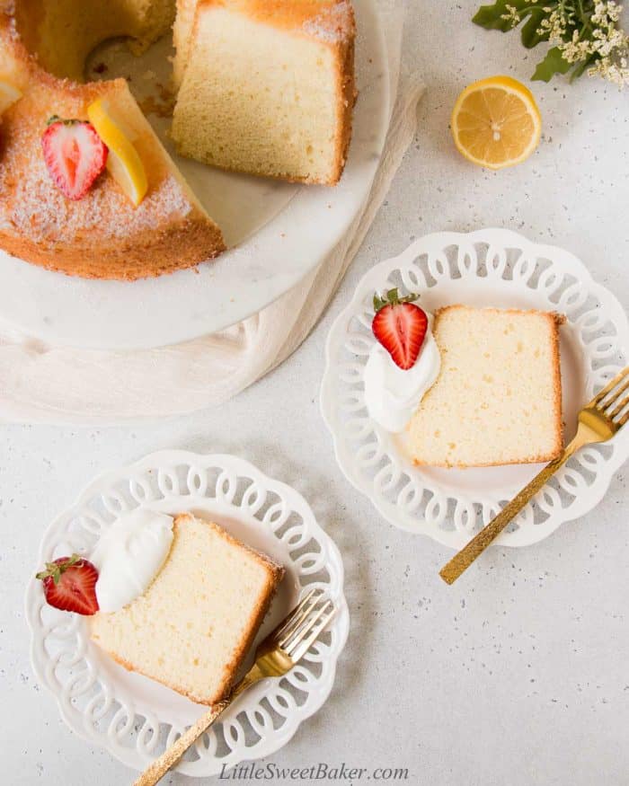 Two slices of lemon chiffon cake on white plates with cream and strawberries.