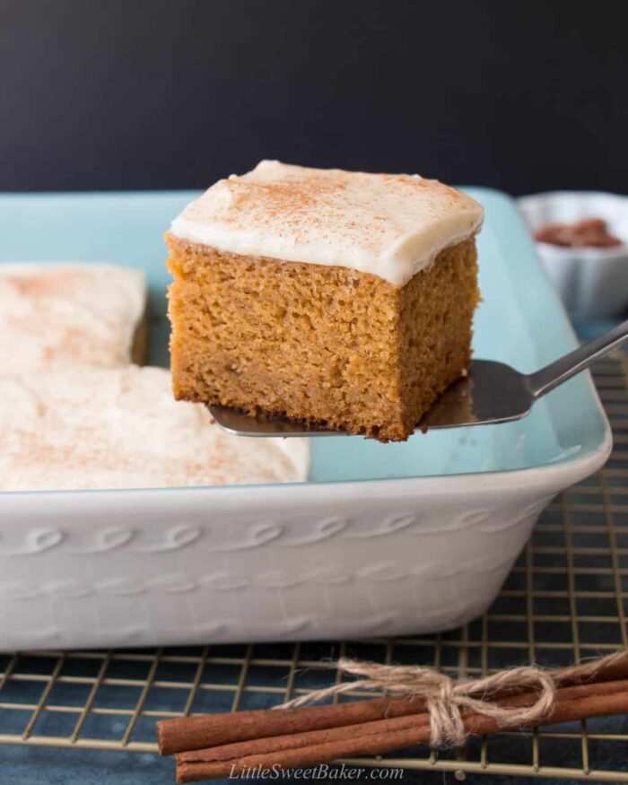 A slice of pumpkin cake with cream cheese frosting being lifted out of cake pan.