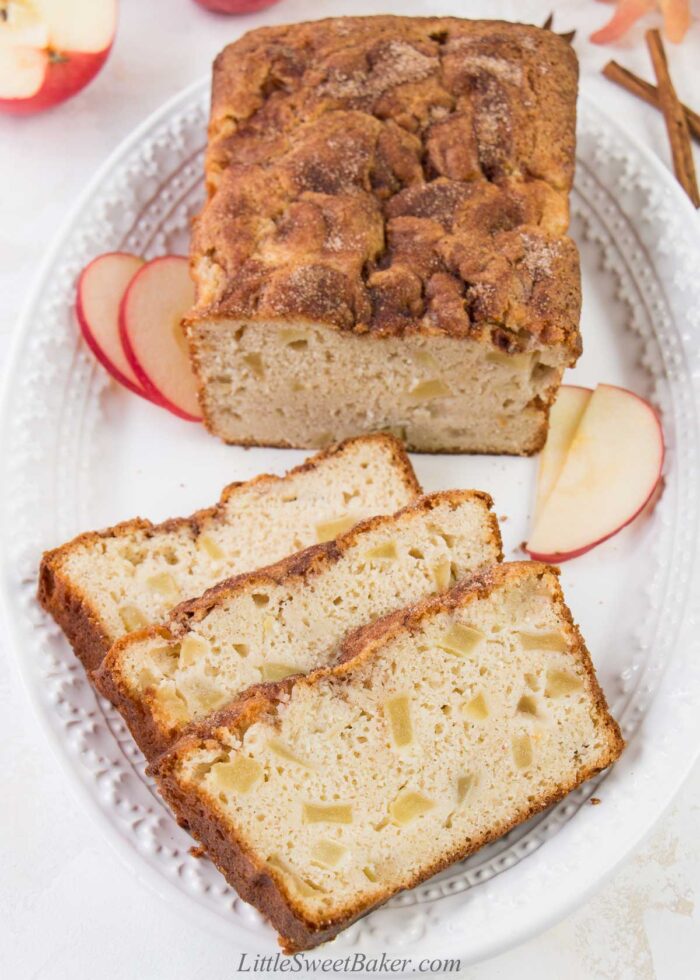 A loaf of apple bread on a white serving plate with three slices cut.