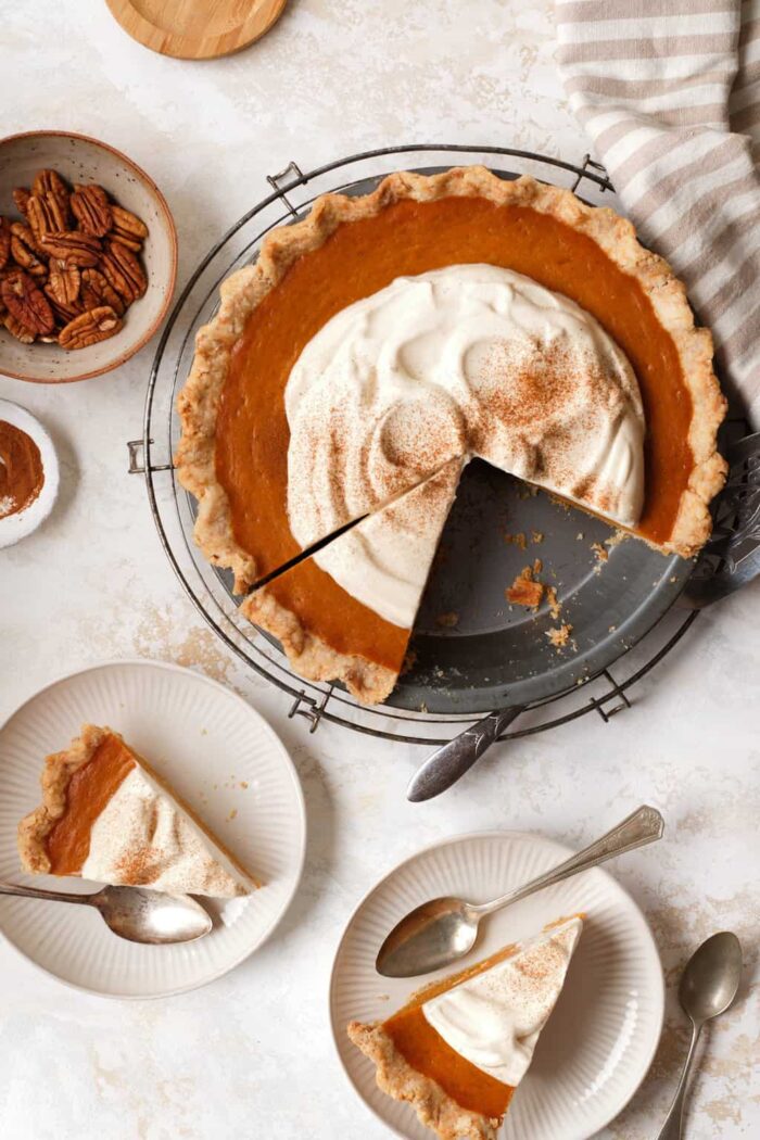 pumpkin pie topped with whipped cream and cinnamon with two slices on plates