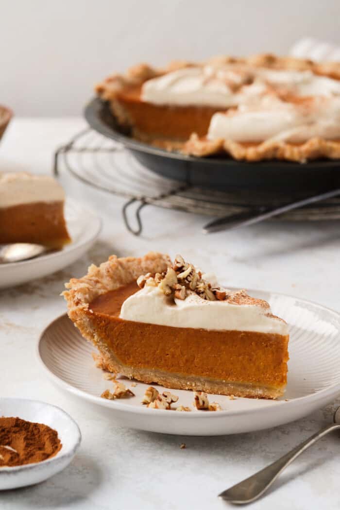 A slice of pumpkin pie with whipped cream and pecans on a plate.