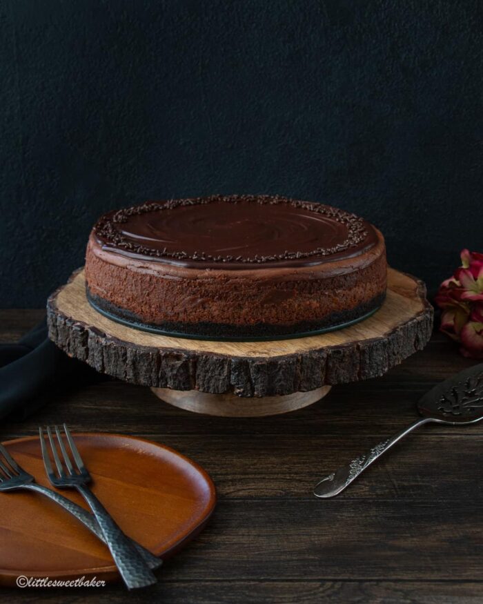 A triple chocolate cheesecake on a wooden cake stand