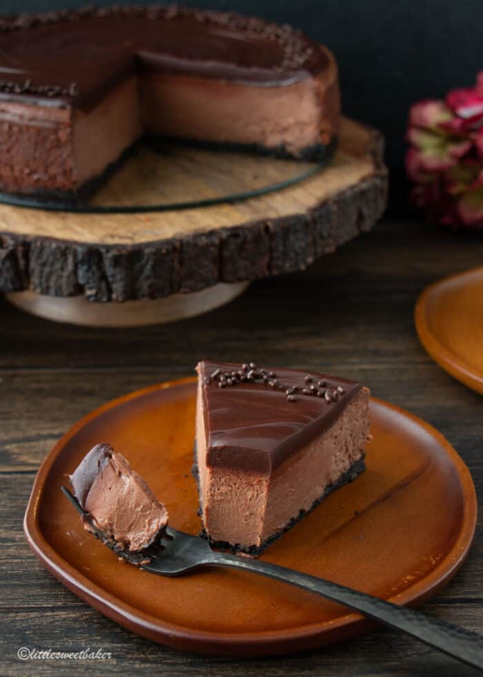 A slice of chocolate cheesecake on a wooden plate with a piece on a fork.
