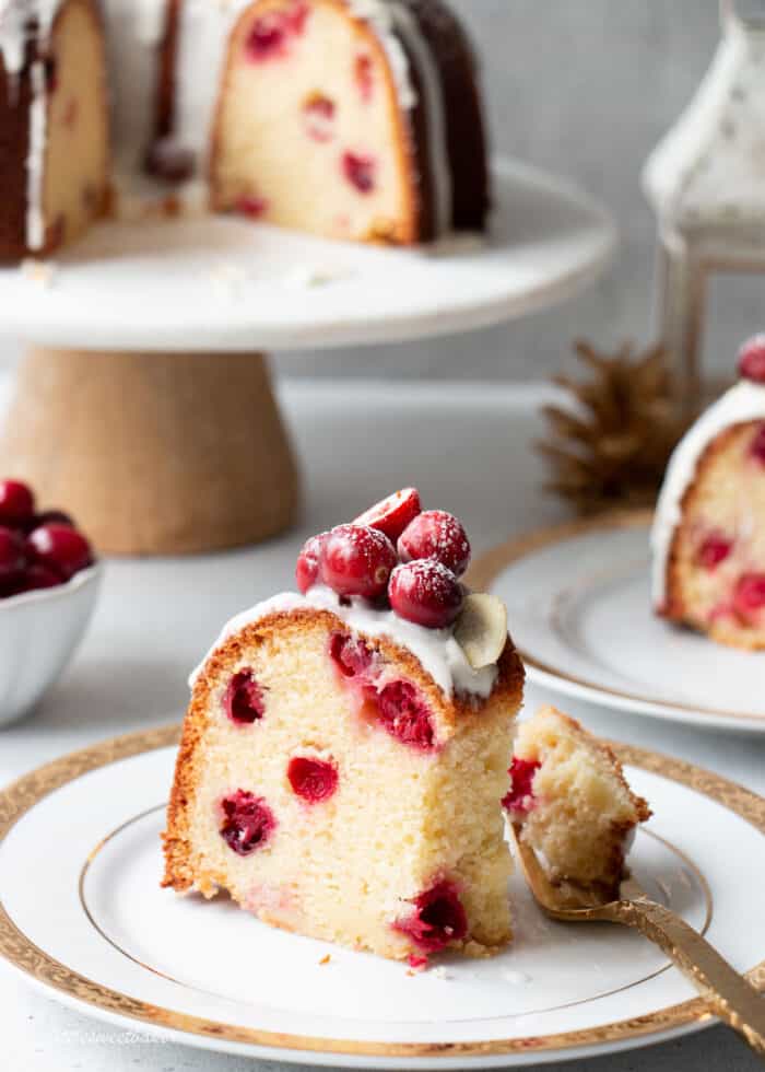 A slice of cranberry cake on a white and gold plate with a piece on a fork