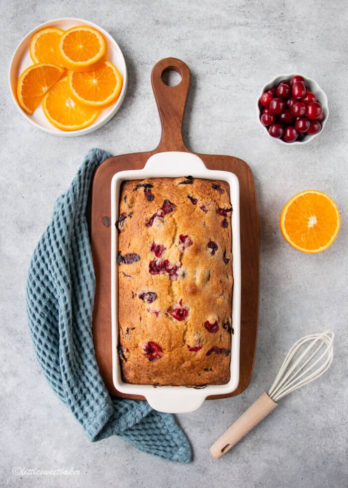 A loaf of cranberry orange bread in a white baking pan on a cutting board.