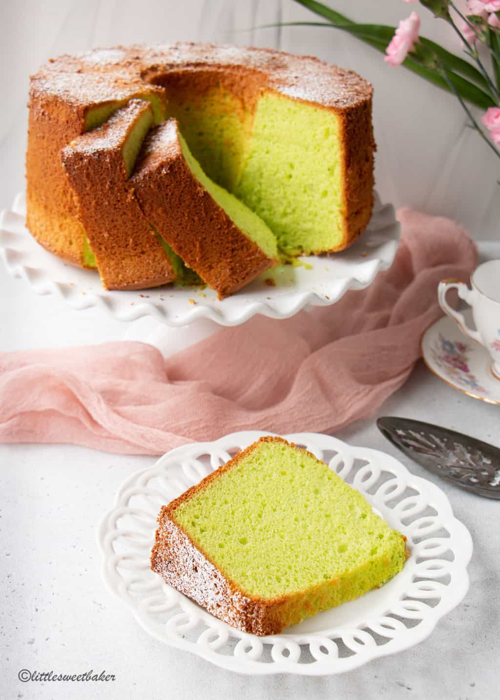 Pandan cake on white cake stand with a slice on a white plate