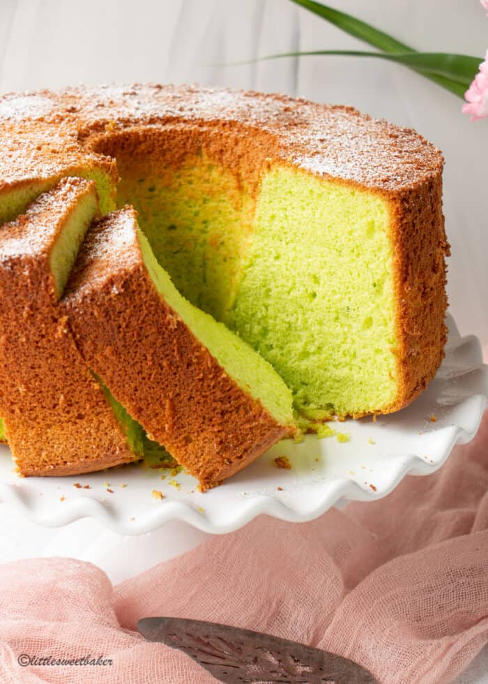 pandan cake on a white cake stand with a few pieces sliced