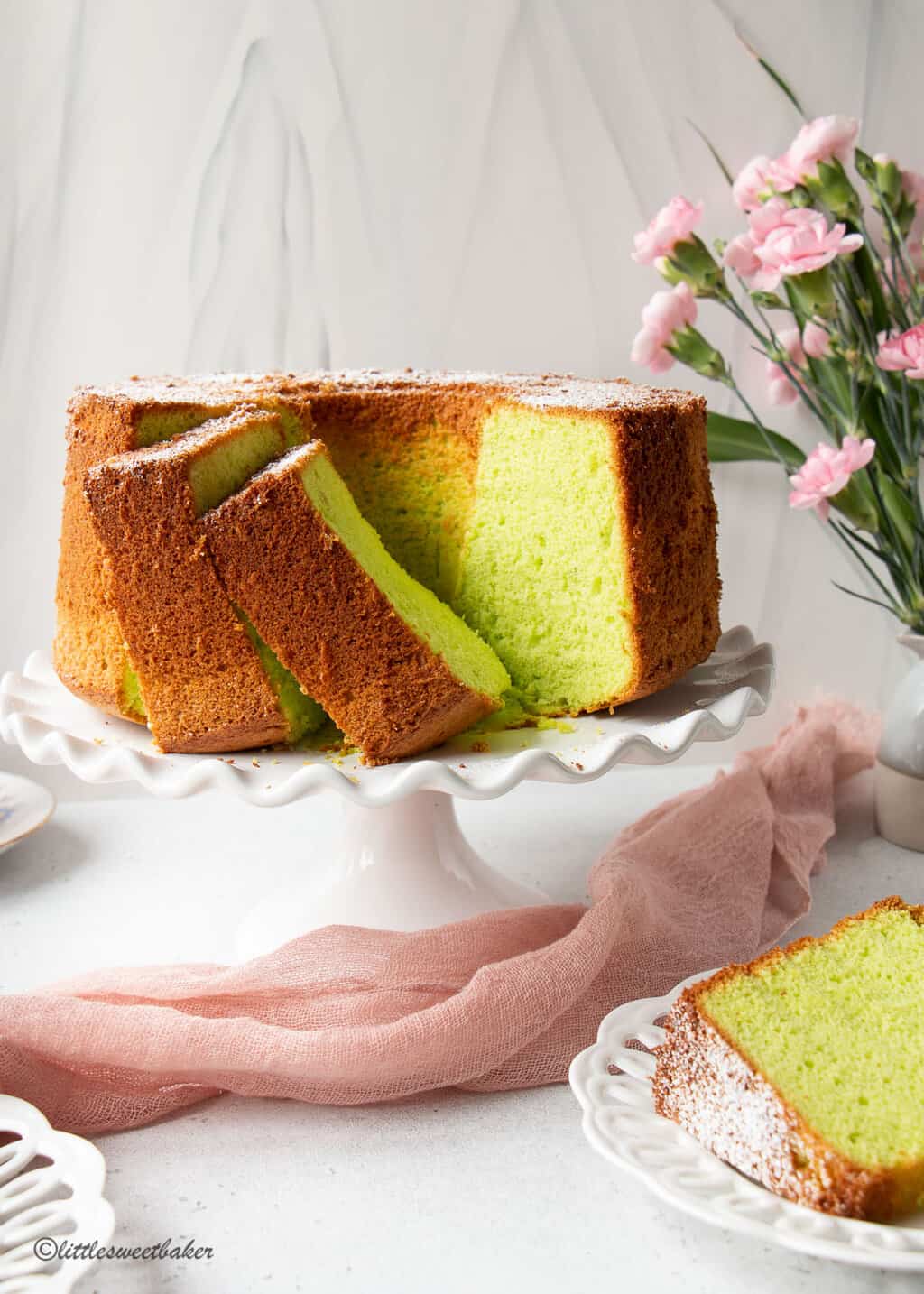 Pandan cake on a white cake stand with pink flowers and pink silk fabric