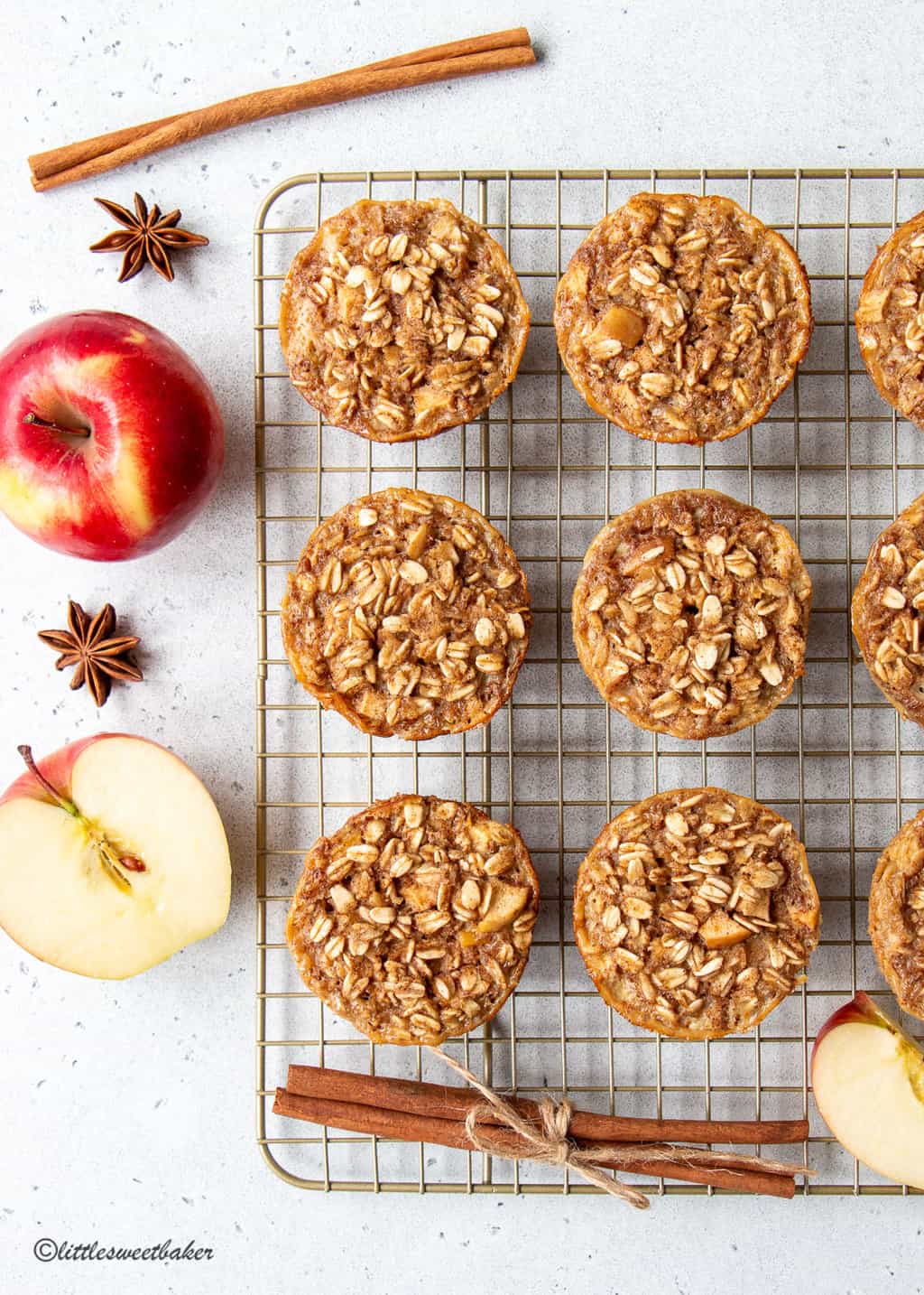 Baked apple oatmeal cups on a cooling rack with apples and cinnamon sticks.