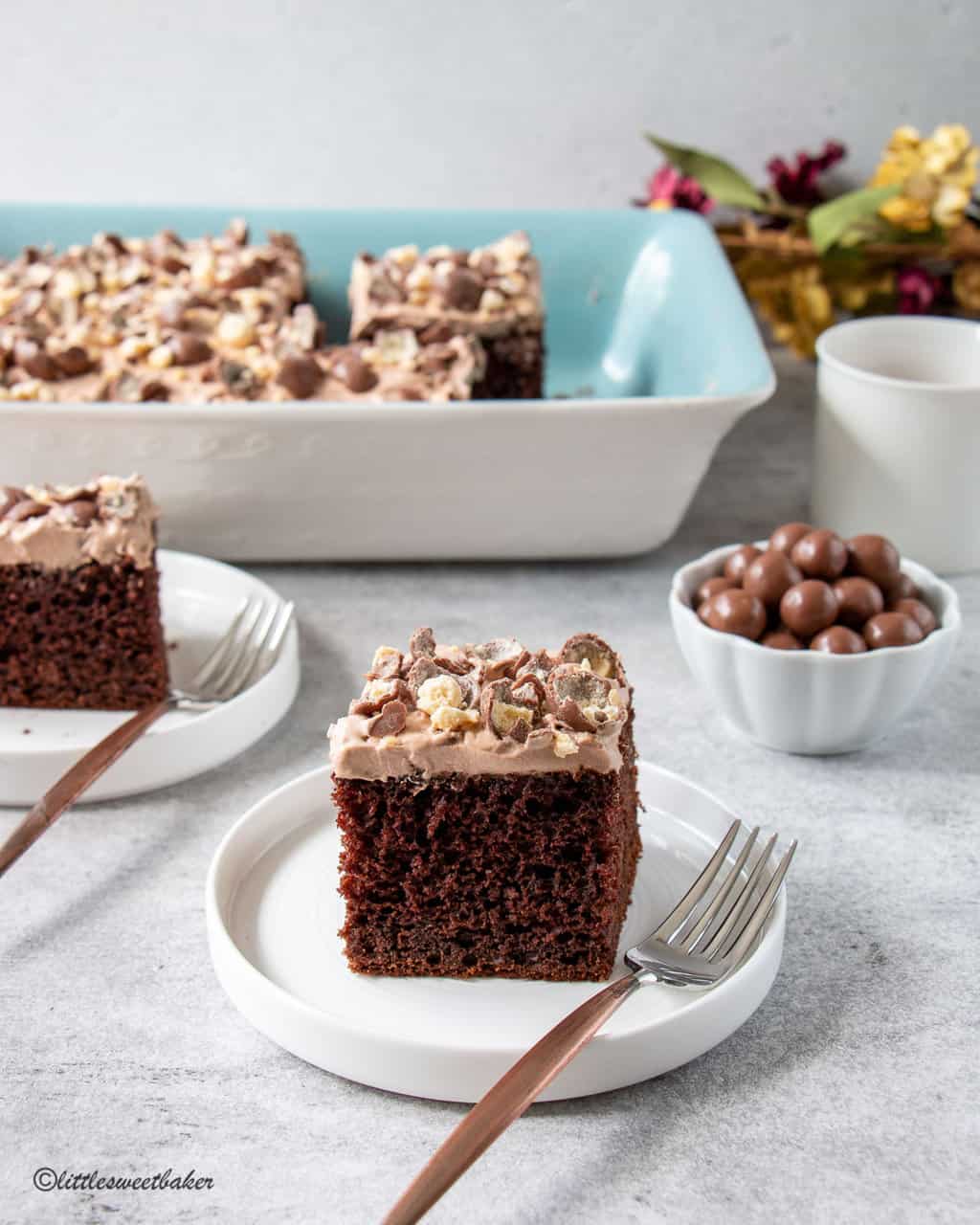 A slice of chocolate malt cake with whipped cream frosting on a white plate with a copper fork.