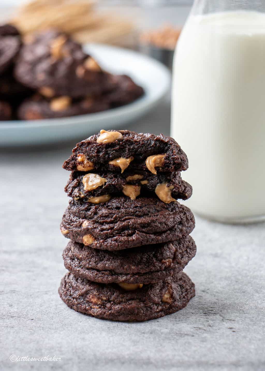 A stack of chocolate peanut butter chip cookies with a glass of milk in the background.