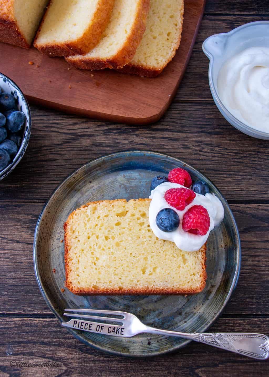 A slice of French yogurt cake on a blue plate with whipped cream and berries.