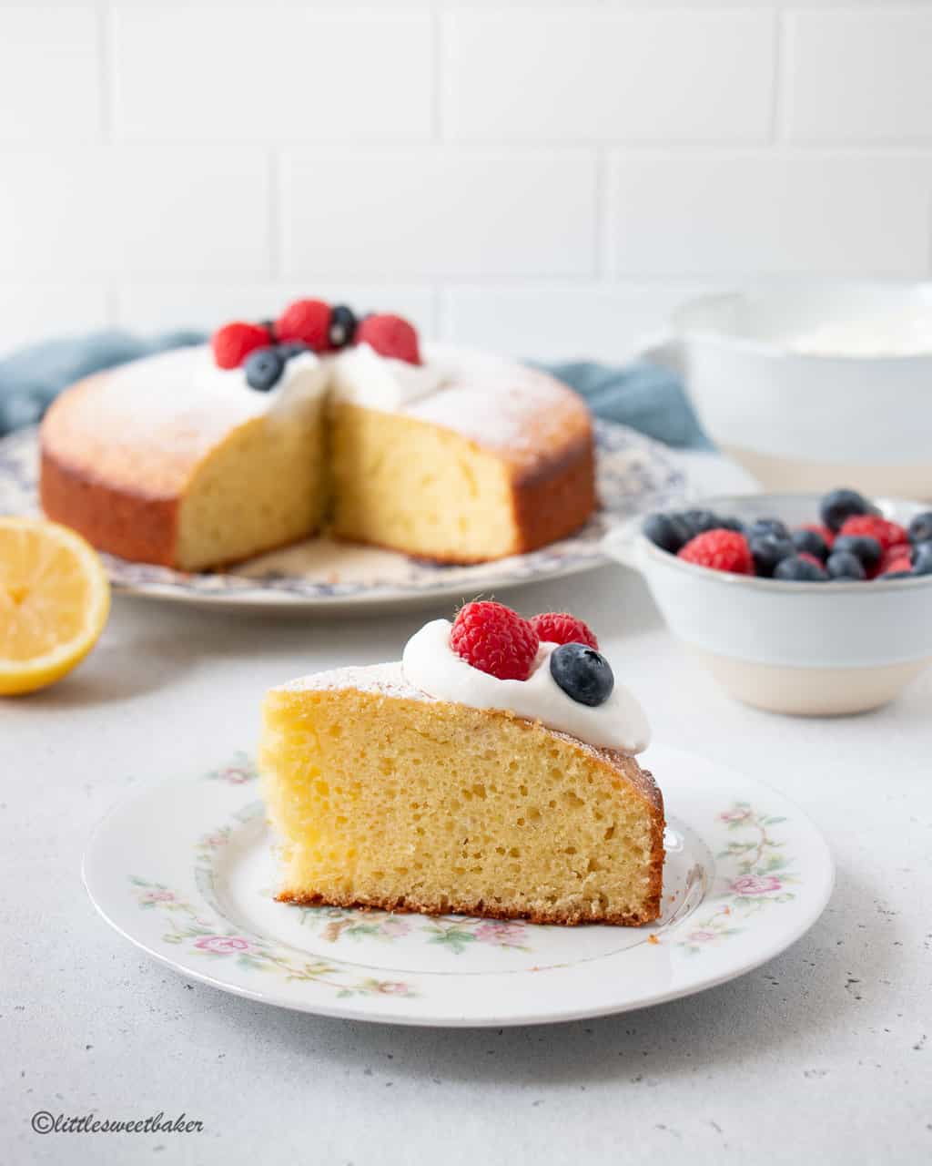 A slice of olive oil cake topped with berries and whipped cream on a floral plate.