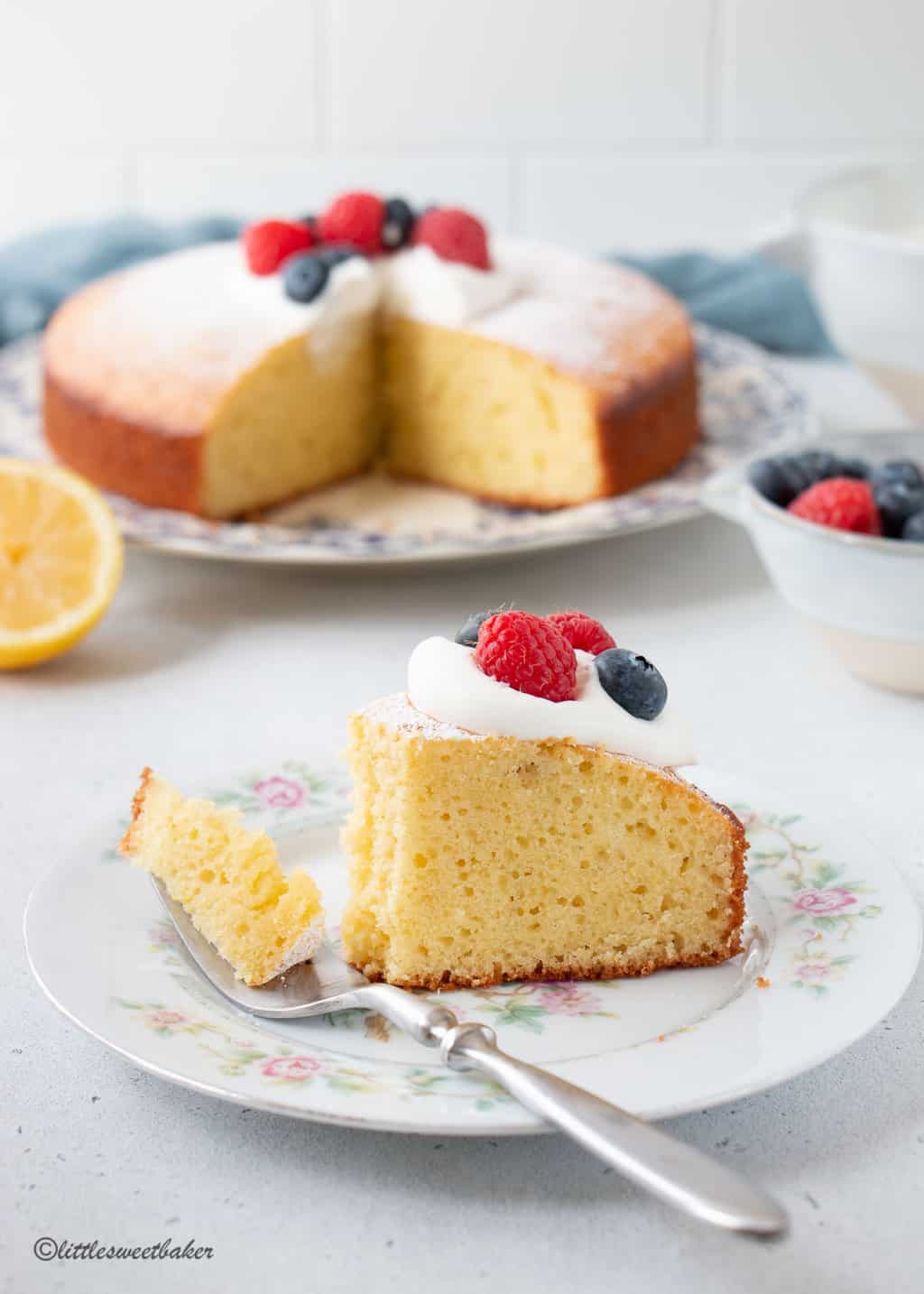 A slice of lemon olive oil cake topped with whipped cream and berries with a piece on a fork.