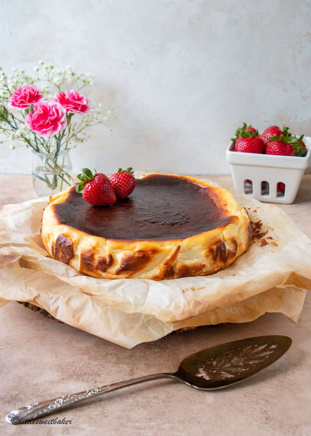 A basque cheesecake on parchment paper topped with two strawberries.