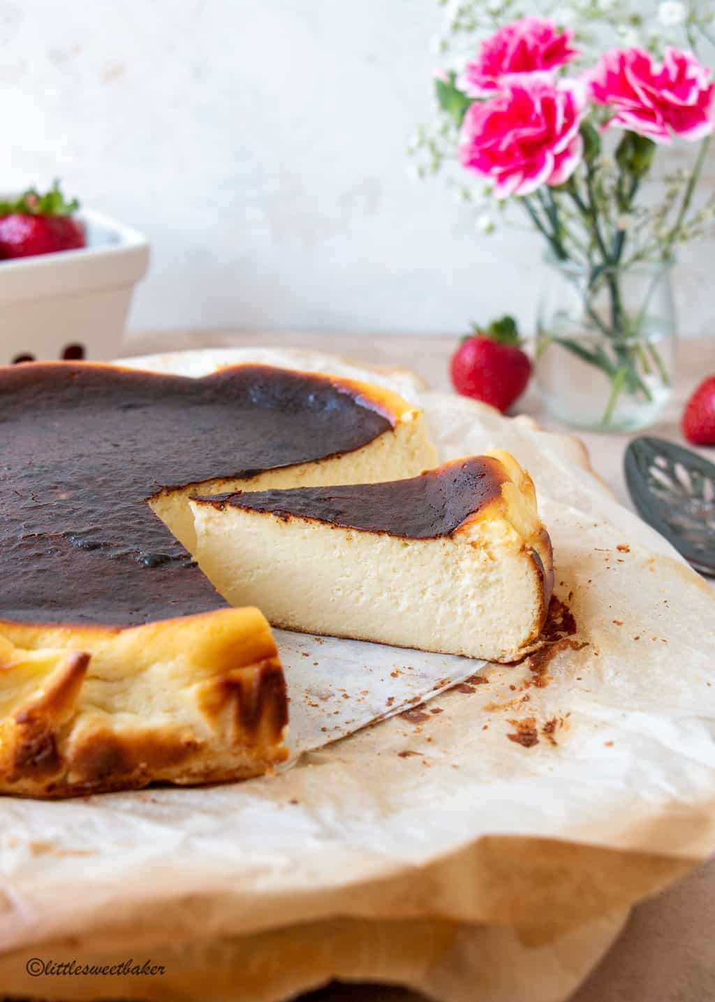 A basque cheesecake on parchment paper with a slice pulled away slightly.