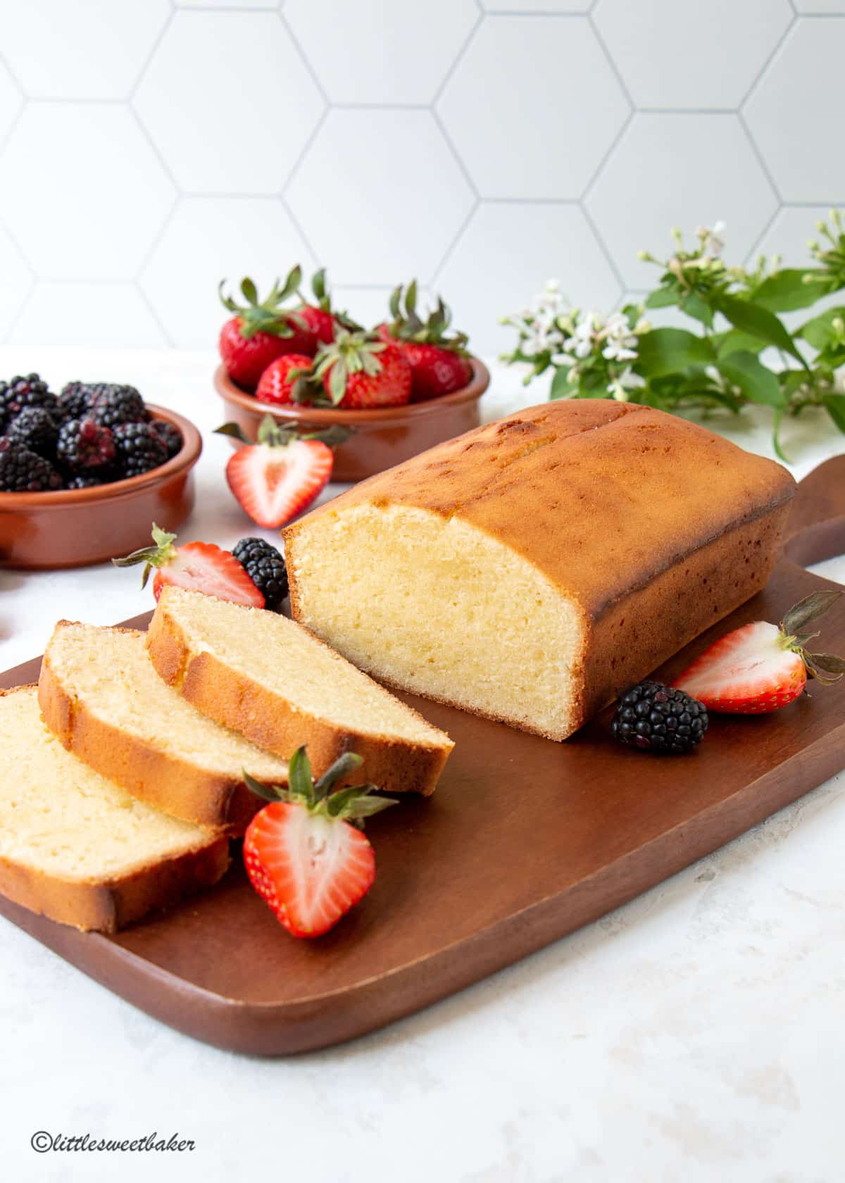 A loaf of cream cheese pound cake on a cutting board with three slices cut and berries.