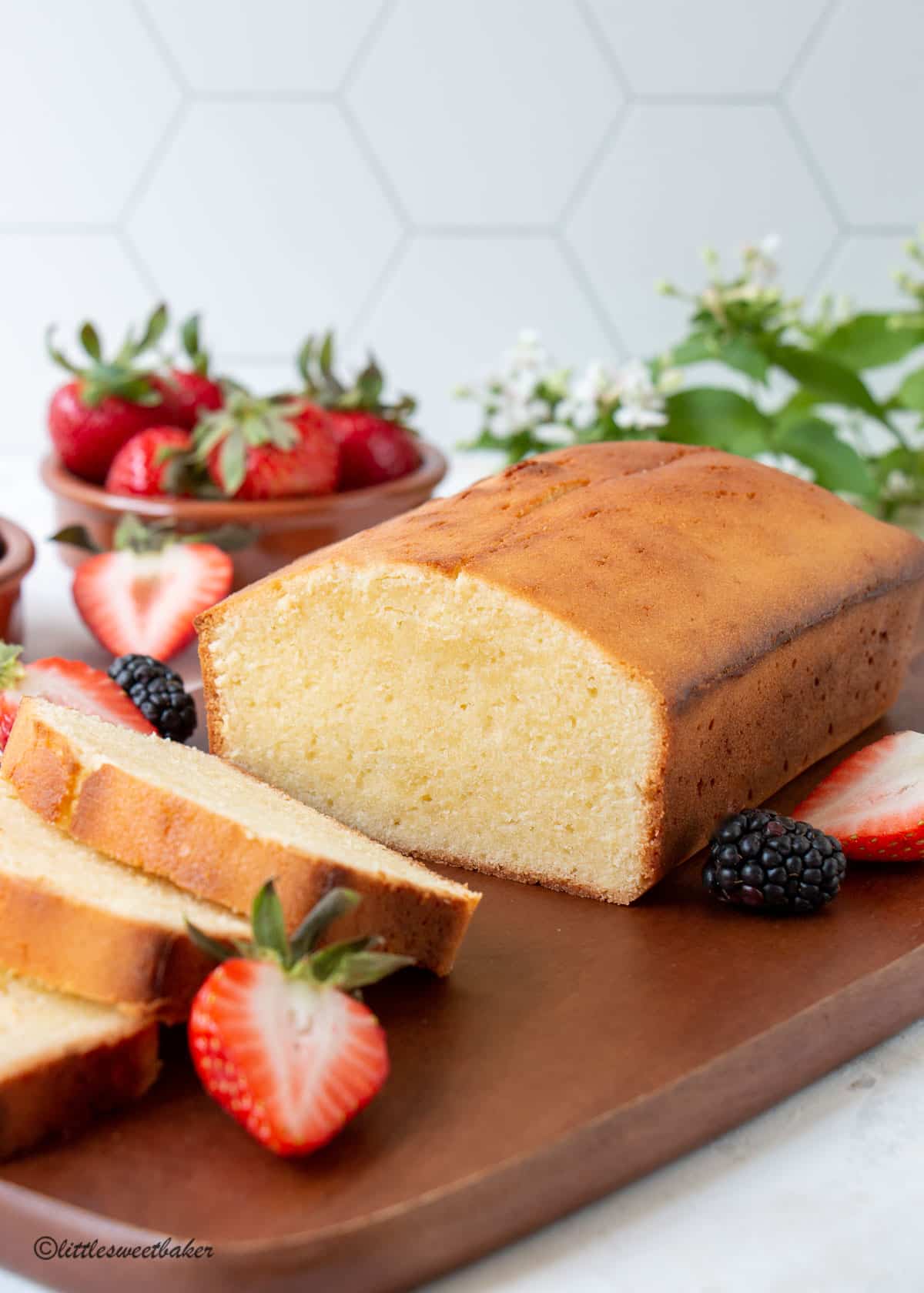 A loaf of cream cheese pound cake on a wooden cutting board with berries.