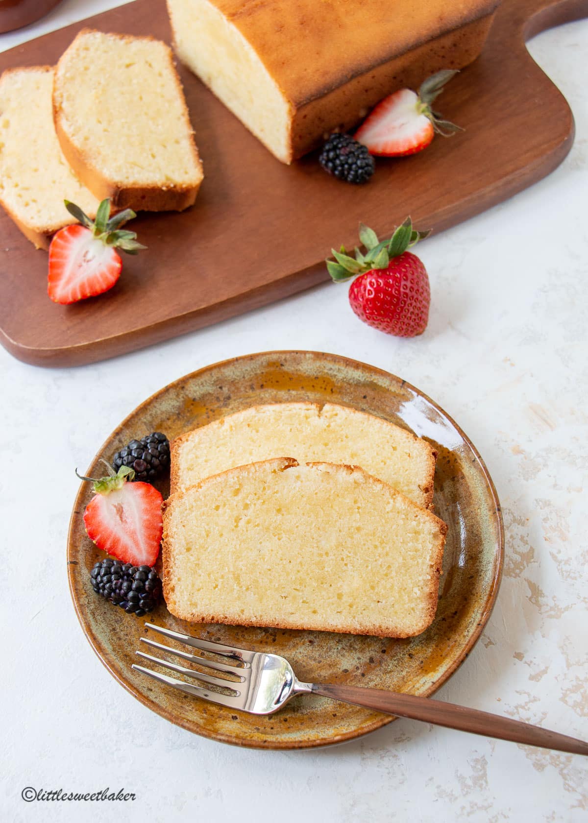 Two slices of cream cheese pound cake on a rustic brown plate with berries.