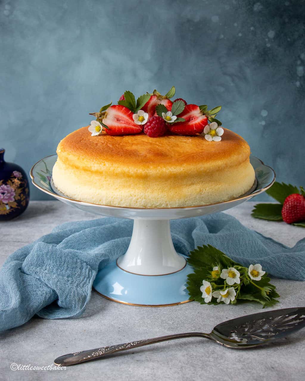 Japanese cheesecake topped with red berries in a blue and white cake stand.