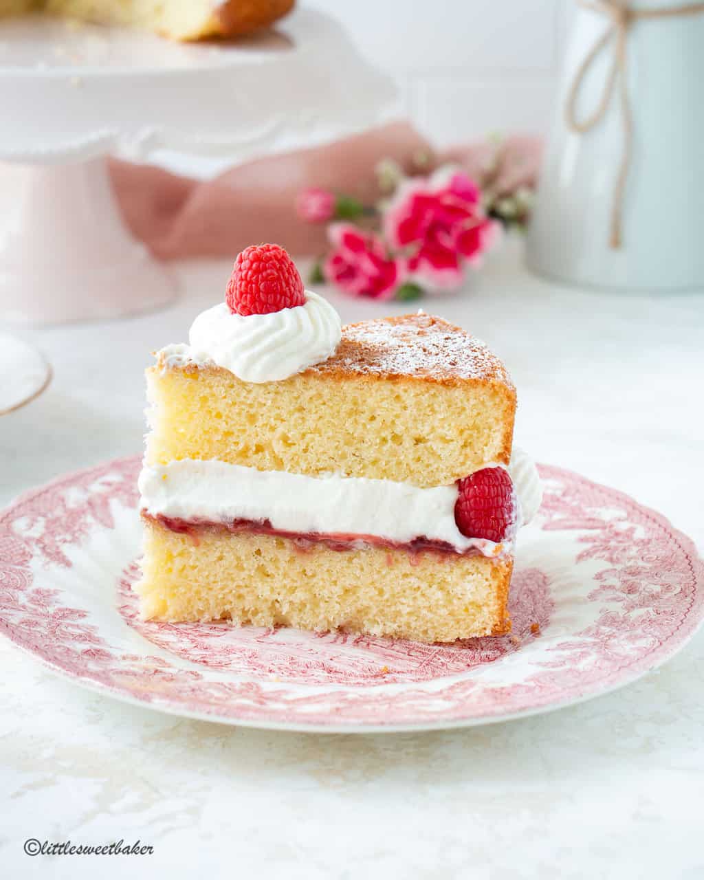 A slice of Victoria sponge cake on a pink vintage plate.