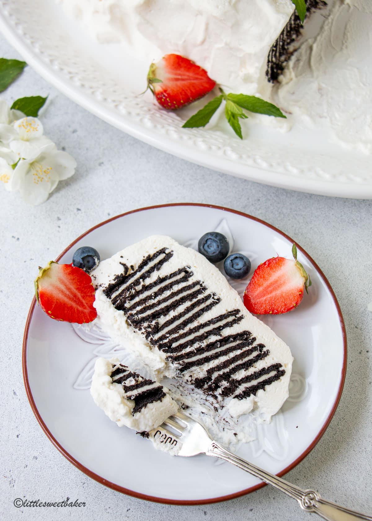 A slice of icebox cake on a plate with strawberries and blueberries.