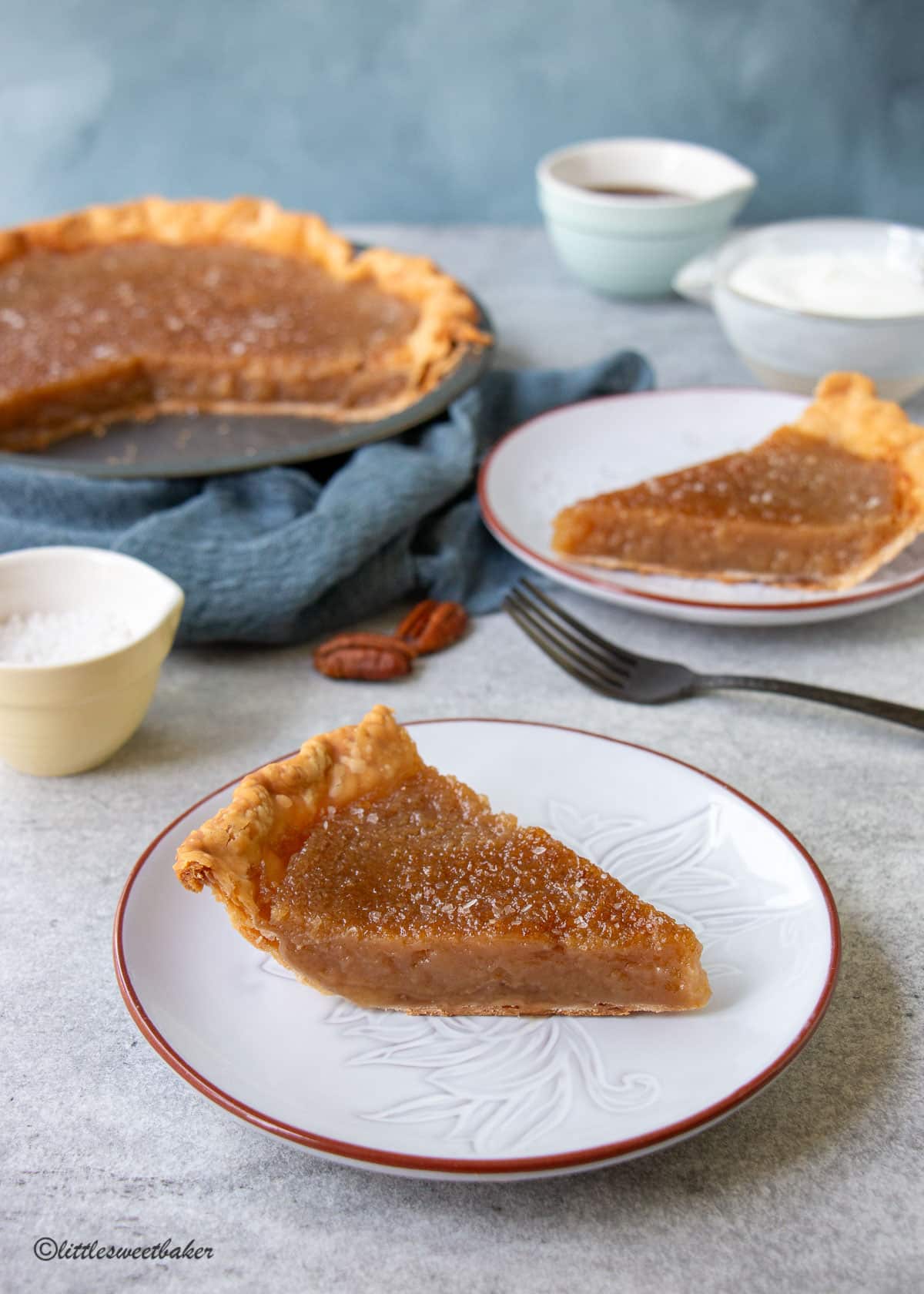 A slice of maple syrup pie on a plate with another slice in the background along with the rest of the pie.