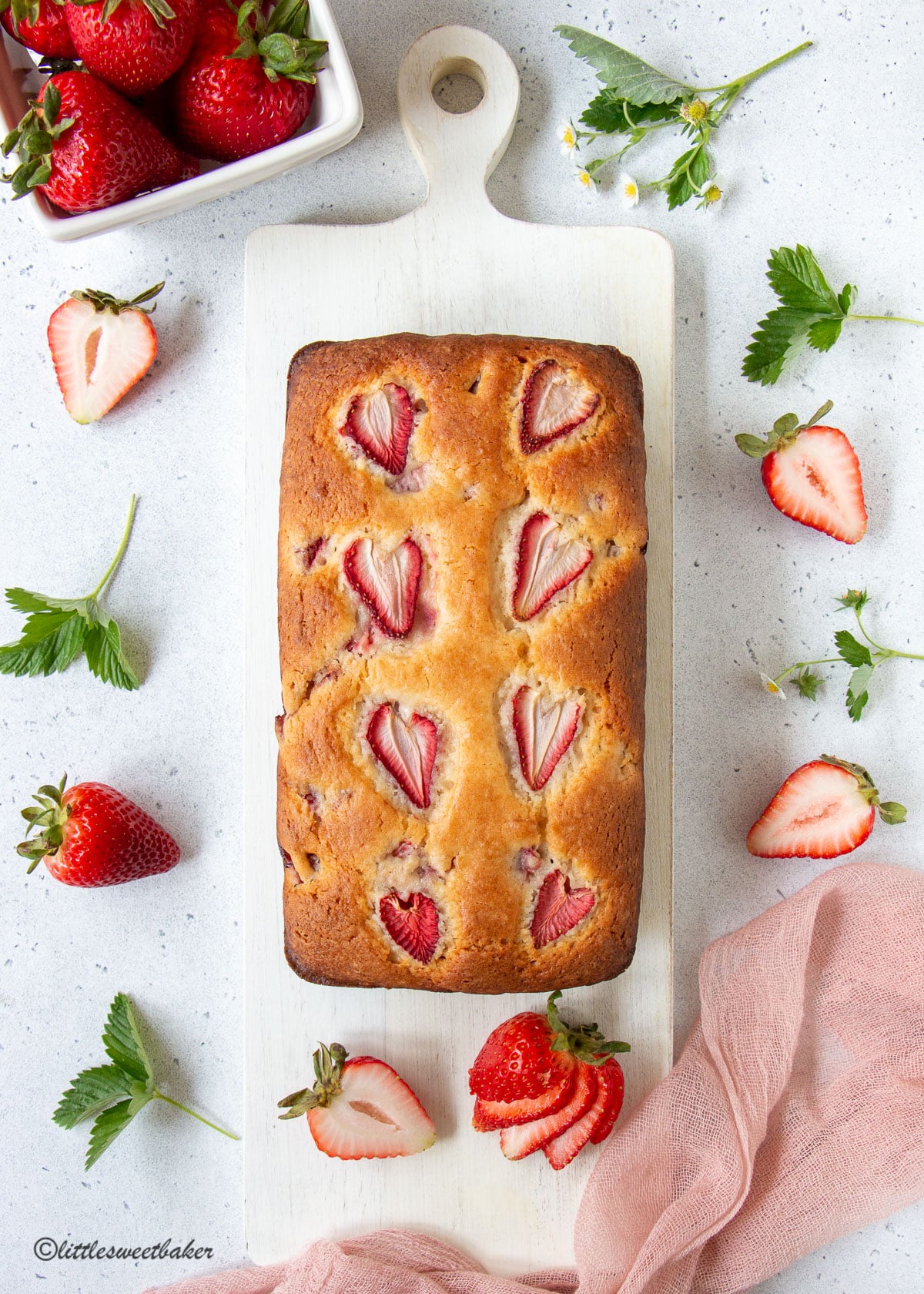A whole loaf of strawberry bread on a white wooden cutting board.