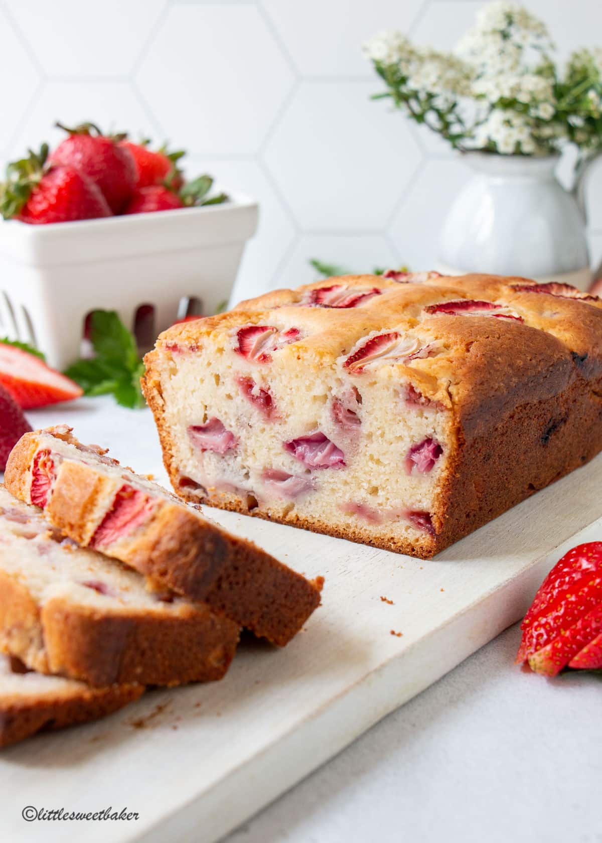 A loaf of strawberry bread on a white cutting board with 3 slices cut.