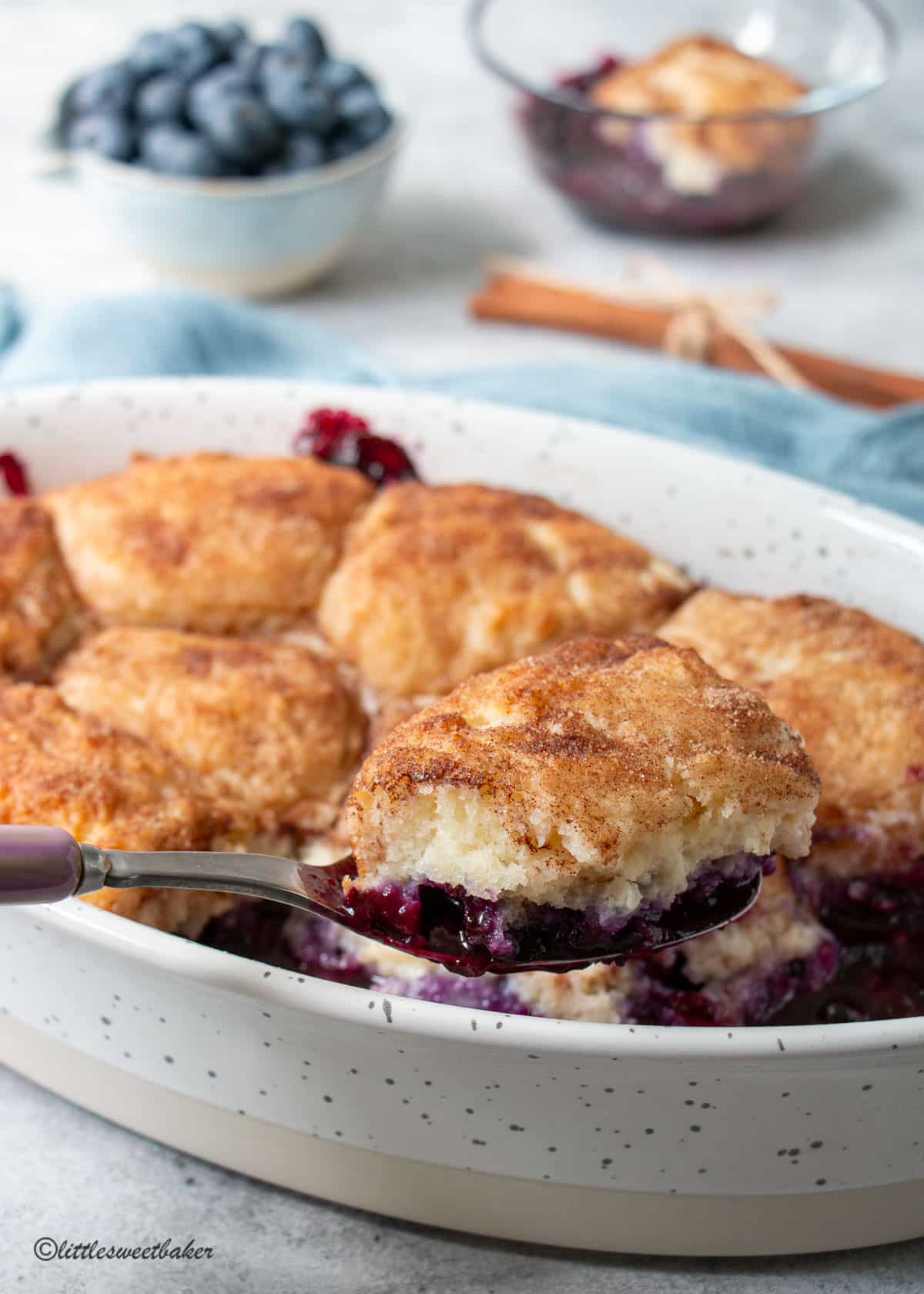An oval dish of blueberry cobbler with a piece being scooped out.
