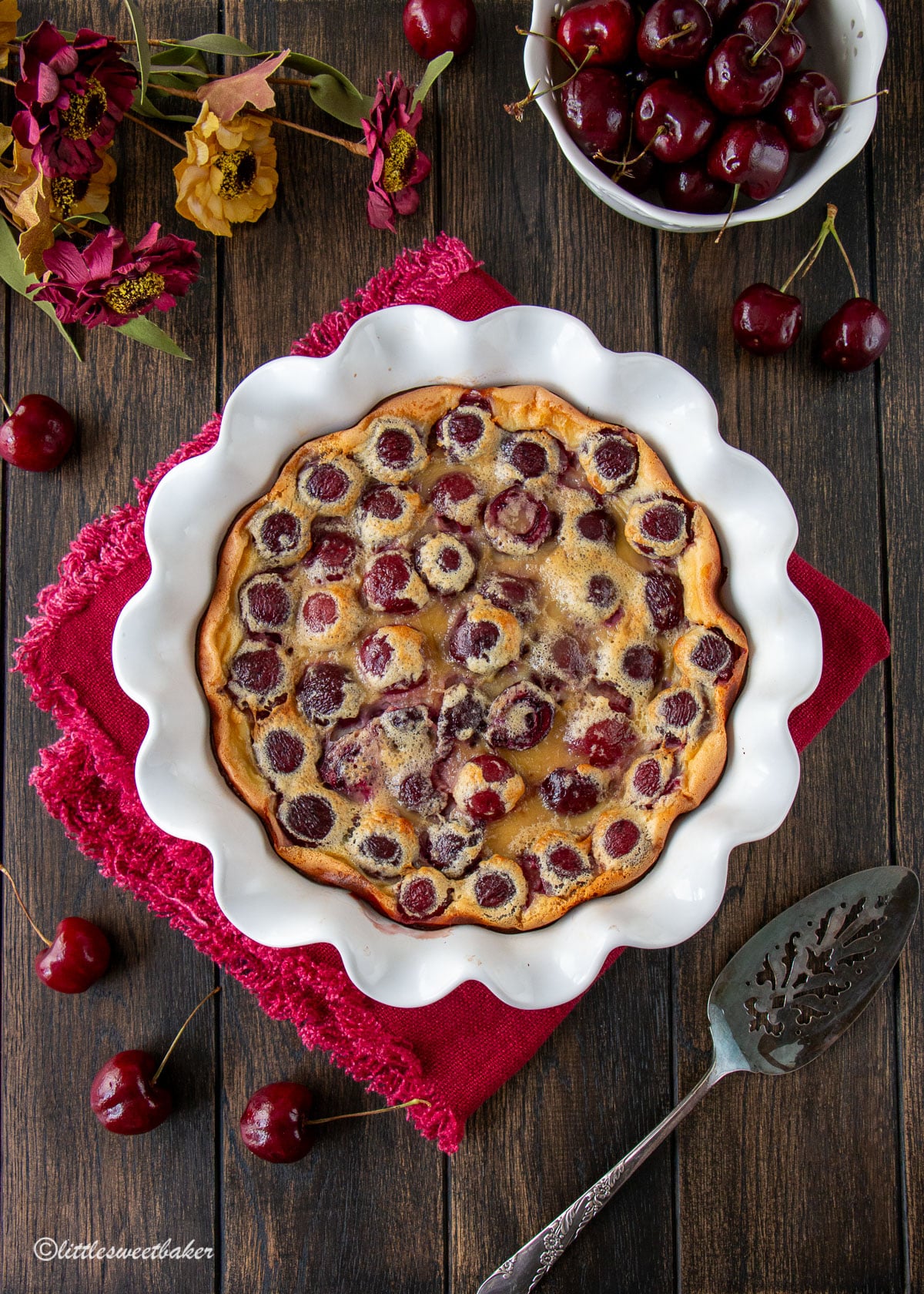 Cherry clafoutis baked in a white pie plate on top of a burgundy napkin.