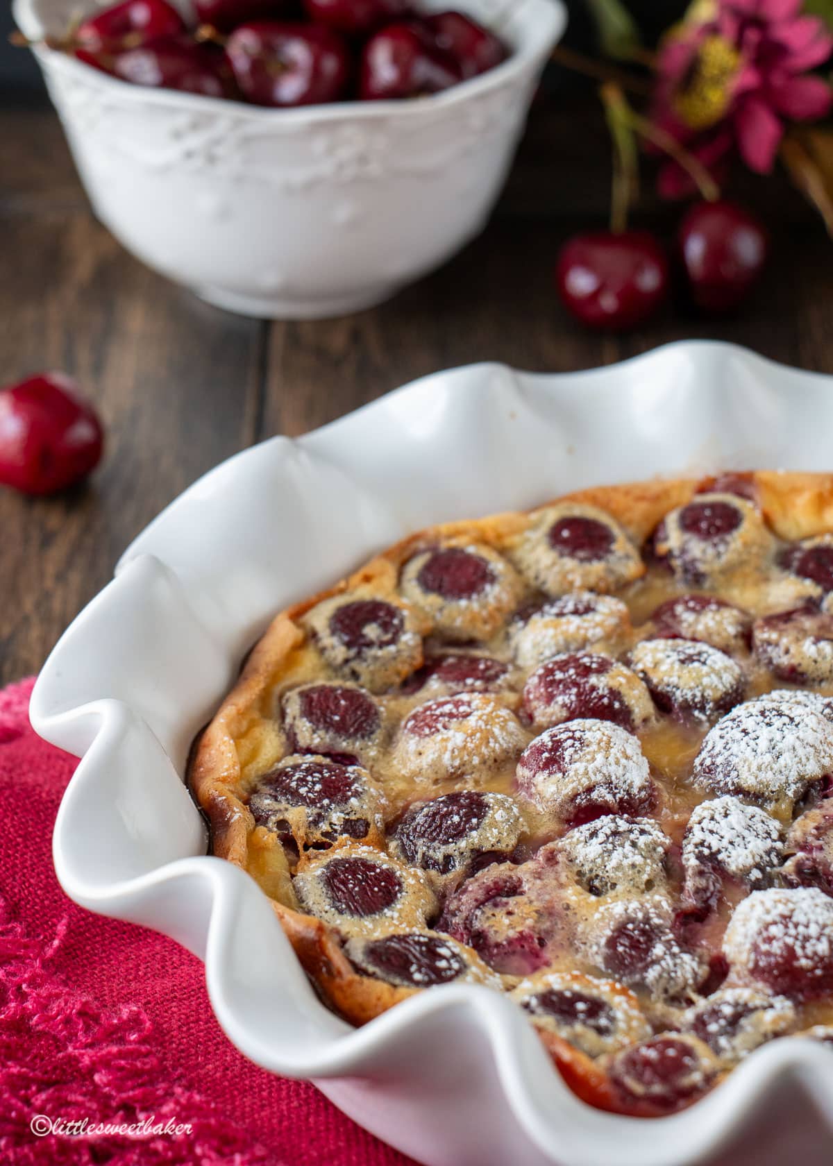 Cherry clafoutis baked in a white pie plate dusted with powdered sugar.