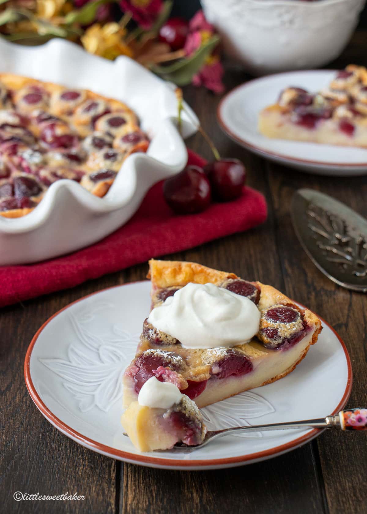 A slice of cherry clafoutis topped with whipped cream with a piece on a fork.