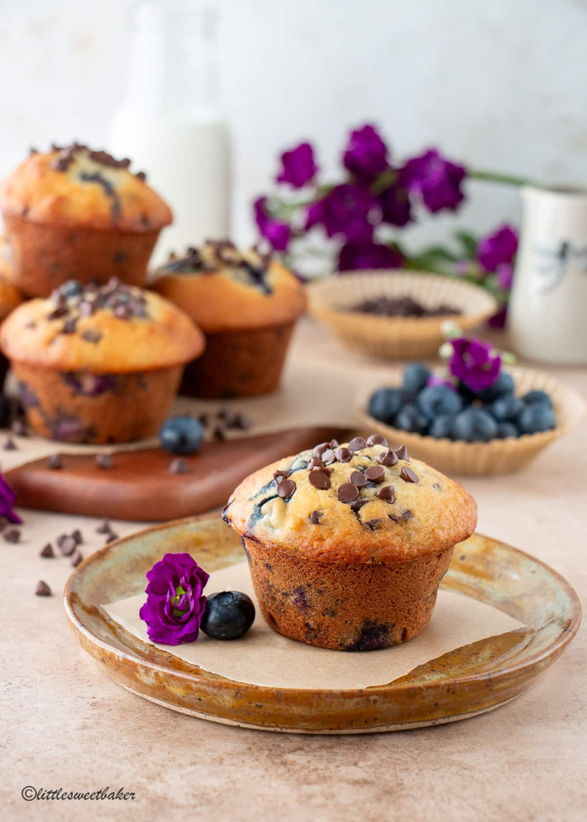 A blueberry chocolate chip muffin on a plate with more muffins on a board in the background.