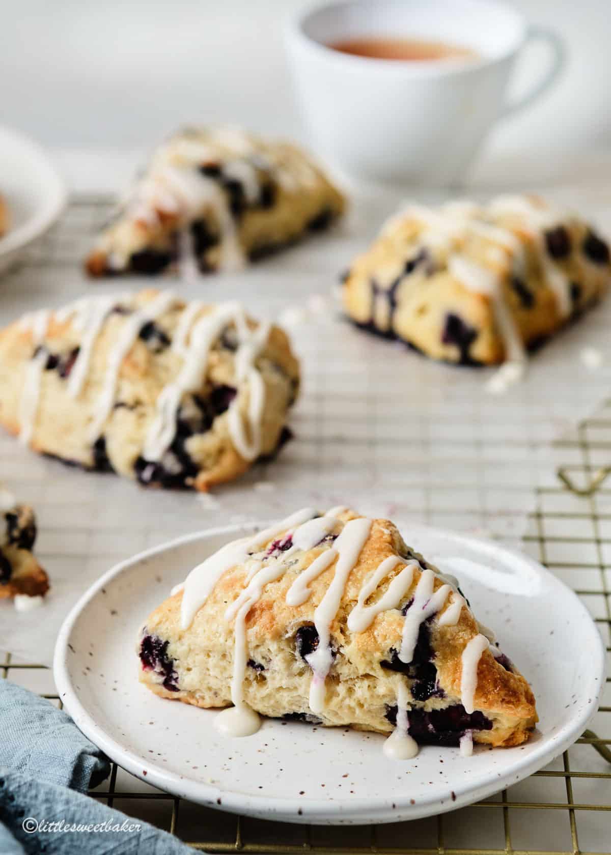A blueberry scone on a plate with other on a cooling rack.
