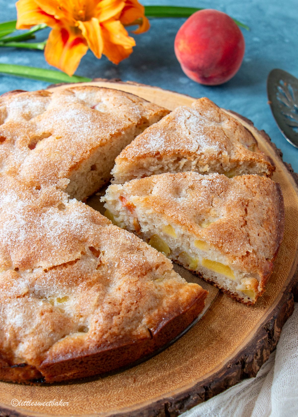 A peach cake on a wooden board with two slices cut.