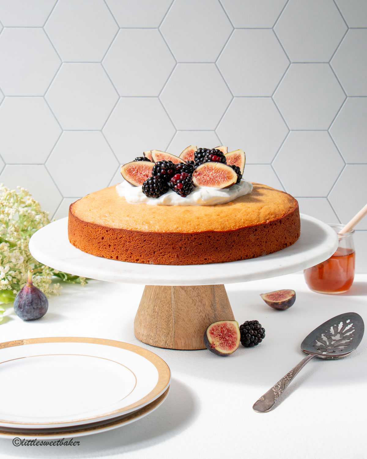A honey cake topped with yogurt and fresh fruit on a marble cake stand.