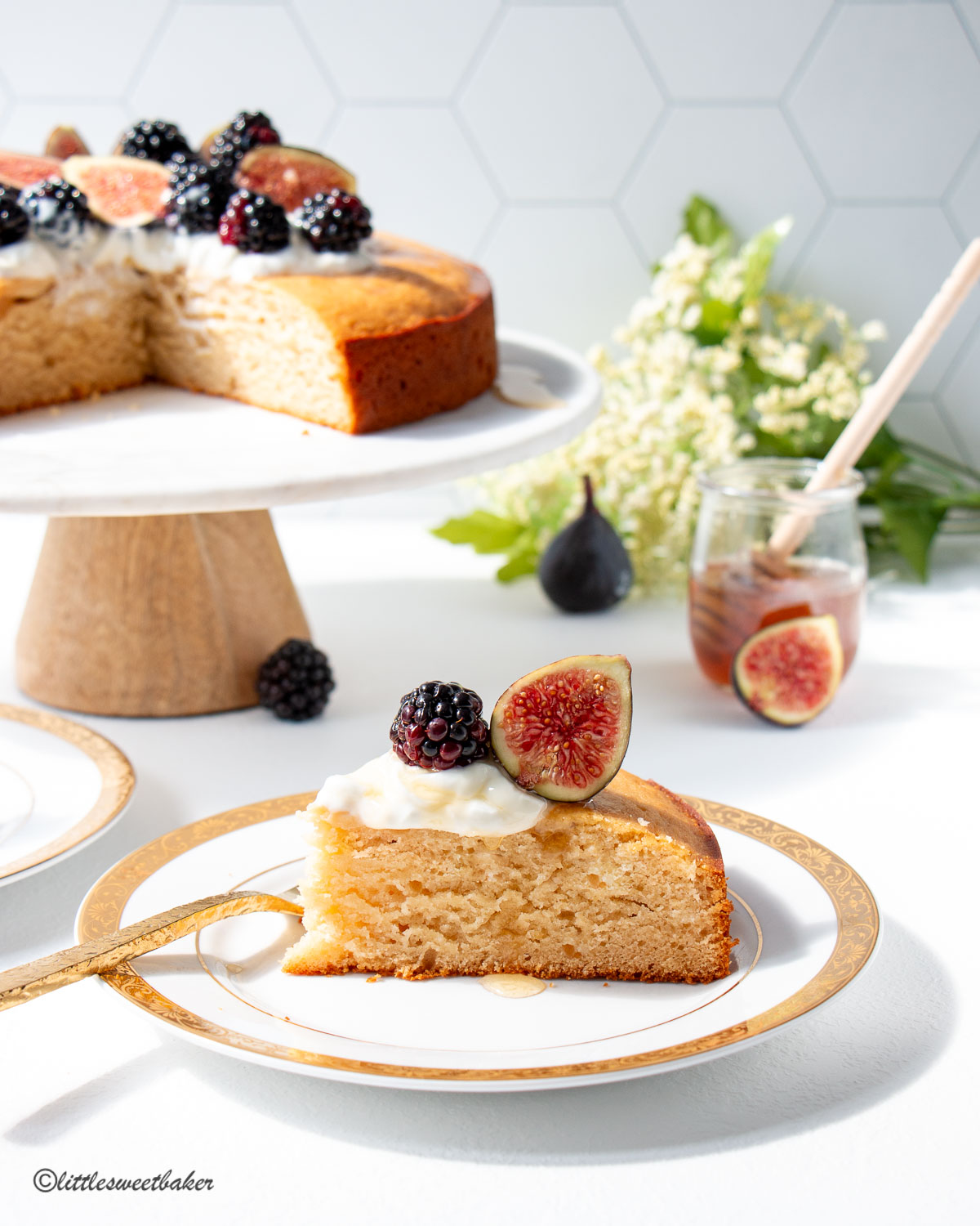 A slice of honey cake topped with yogurt and fruit on a white and gold plate.