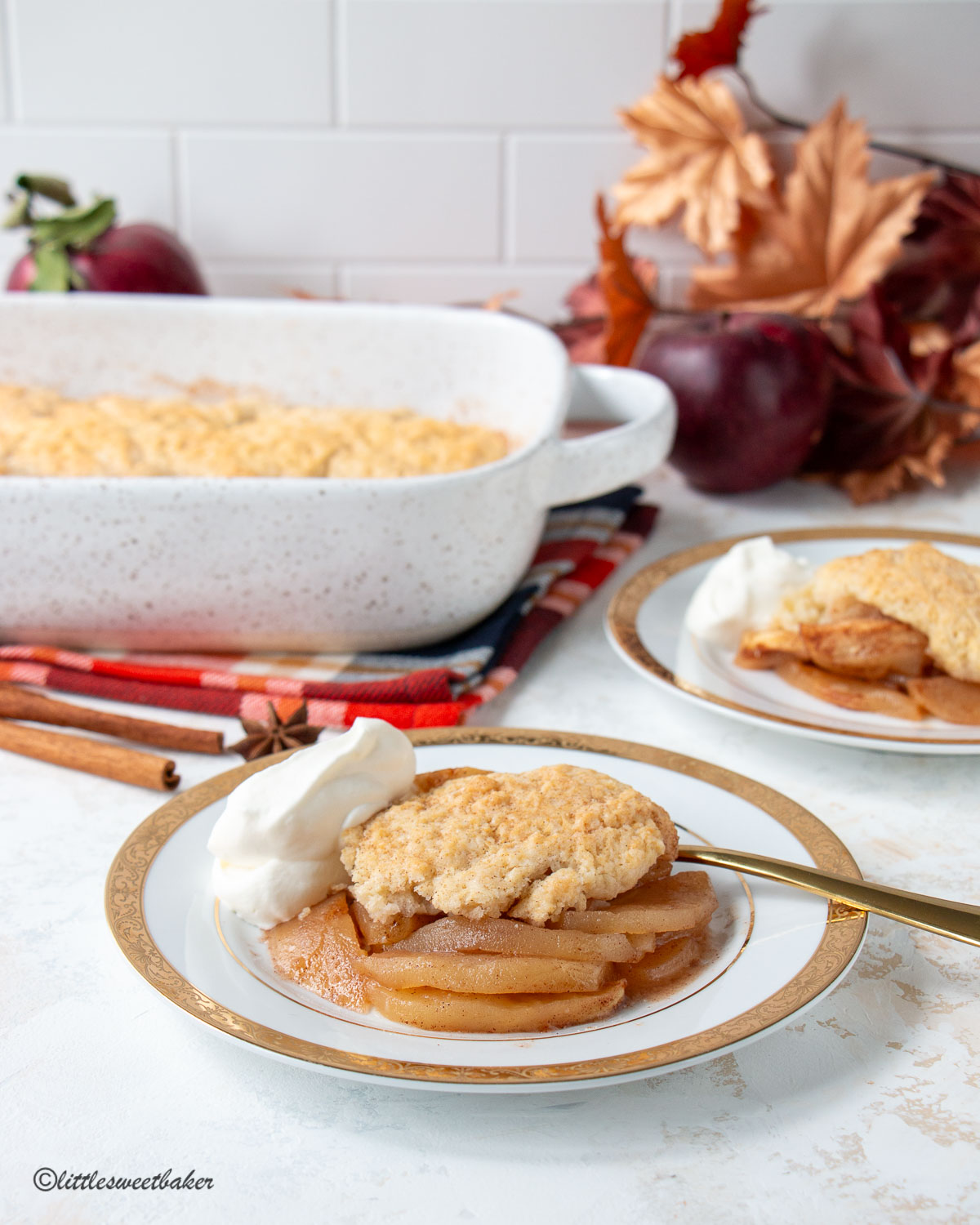 Apple cobbler with whipped cream on a white and gold plate.