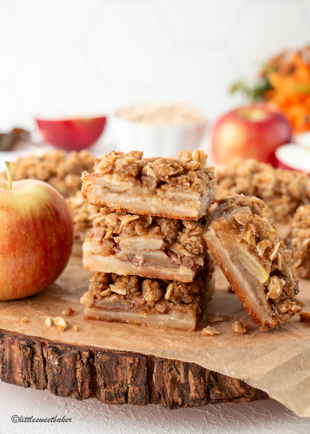 A stack of apple crisp bars beside an apple on wooden board.