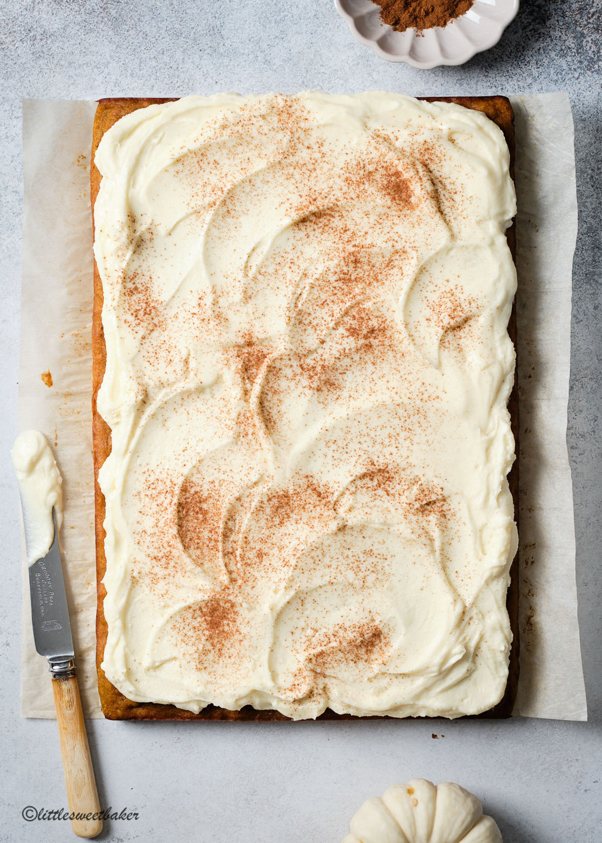A whole pumpkin bar uncut with swirls of cream cheese frosting dusted with cinnamon.