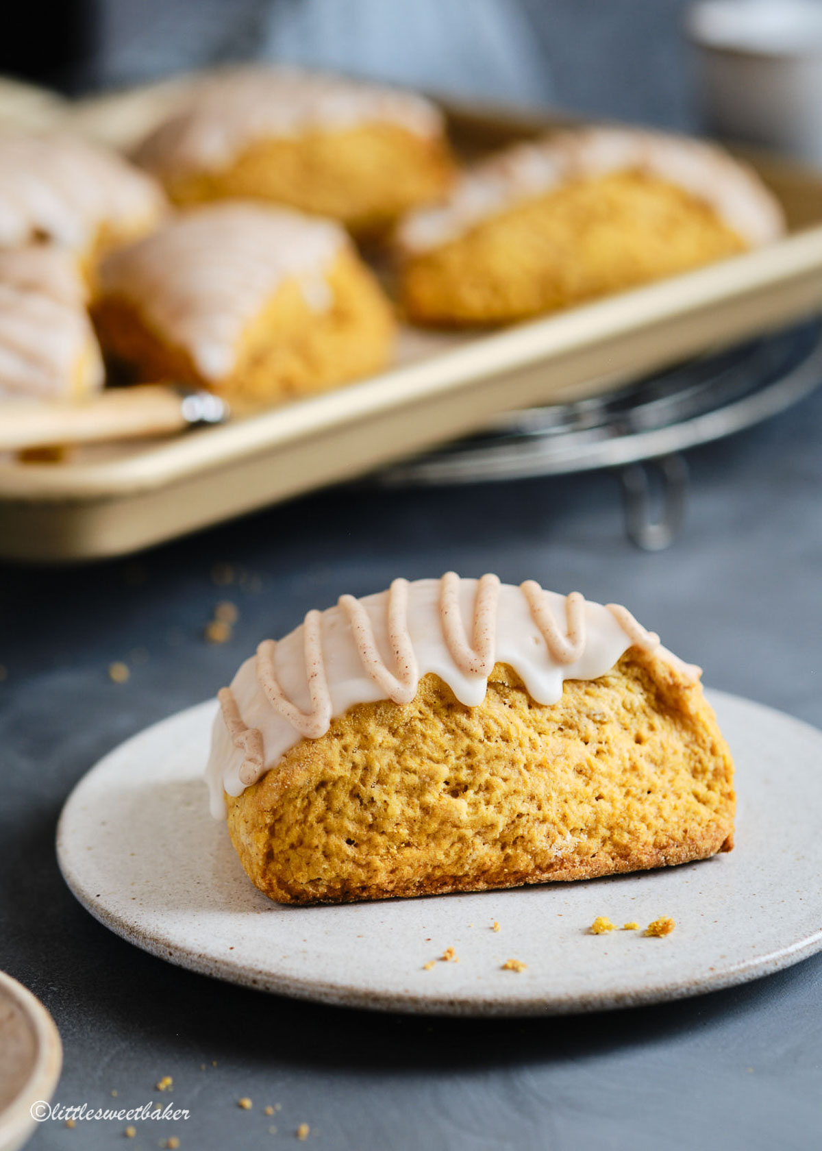 A beautiful pumpkin scone on a plate with the rest on a baking sheet in the background.